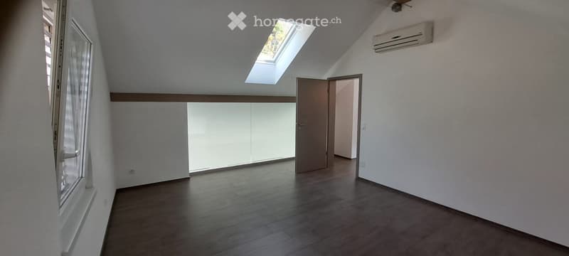 Empty room with wooden flooring, white walls, large window, and skylight. No furniture or equipment present.