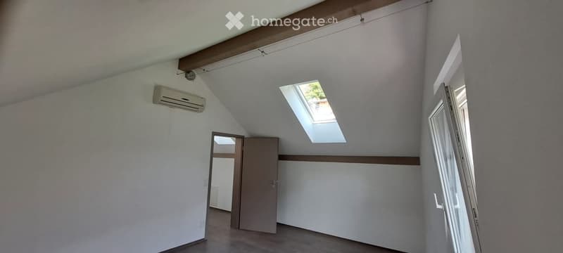 Empty room with white walls, wooden floor, a door, and a skylight window. No furniture or equipment present.