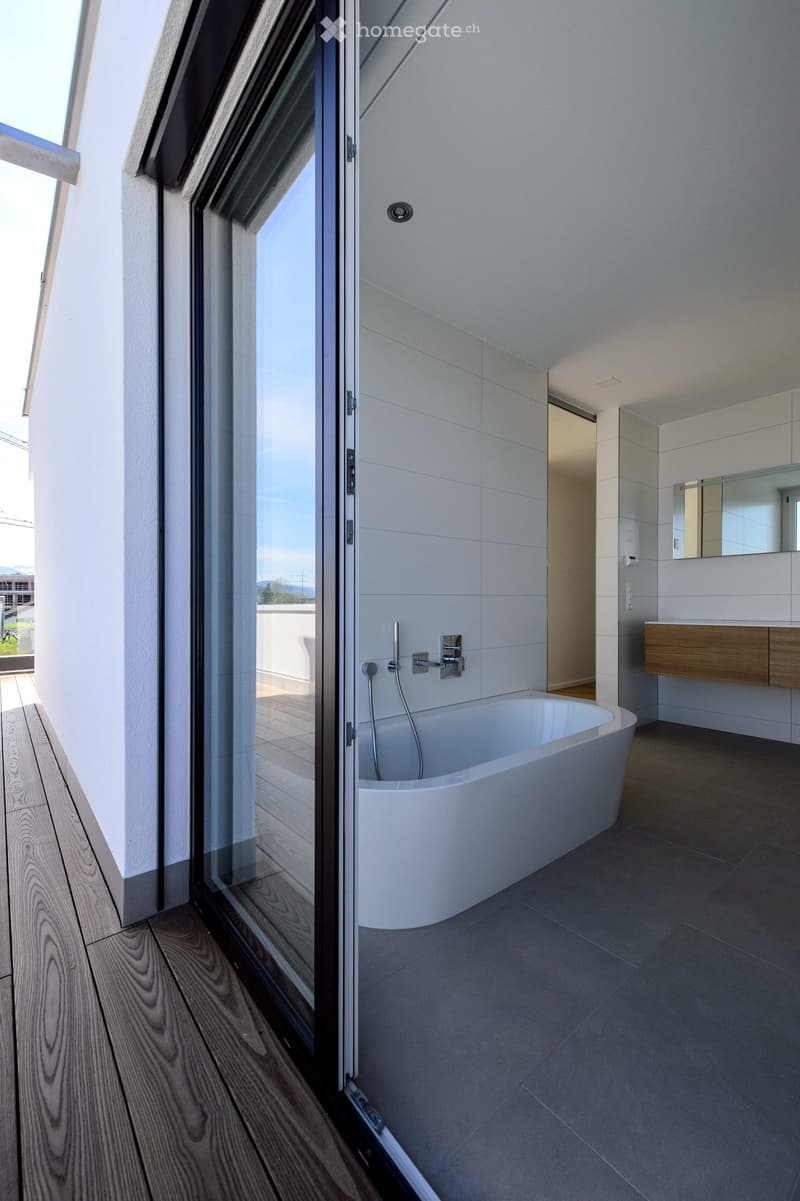 Modern bathroom with a freestanding bathtub, a wooden sink cabinet, and a large mirror. The space features large windows with a view of the outdoors.