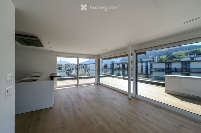 Bright, open-plan room with wooden flooring, large glass sliding doors leading to a balcony, and a scenic mountain view.