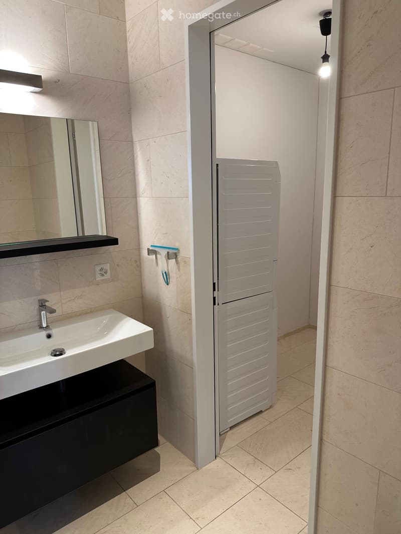 Modern bathroom with a white sink, black cabinet, mirror, and a partially open door leading to another room.
