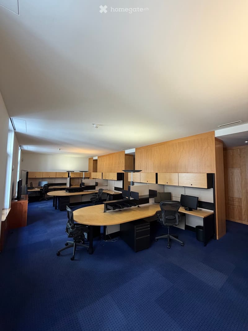 Office space with multiple desks, chairs, computers, and wooden cabinets.