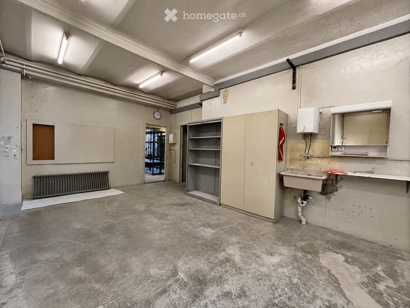 Empty room with concrete floor, exposed pipes, sink, cabinets, and a radiator. No furniture or personal items present.