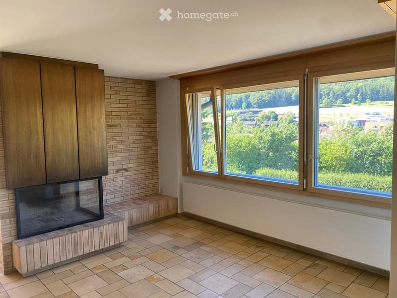 Living room with tiled floor, brick wall, large windows offering a scenic view, and a fireplace.