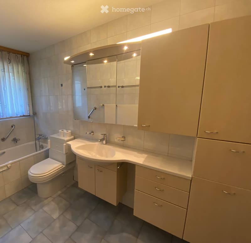 Modern bathroom with a sink, toilet, bathtub, mirror, and built-in cabinets. Features tiled walls and a window with a curtain.