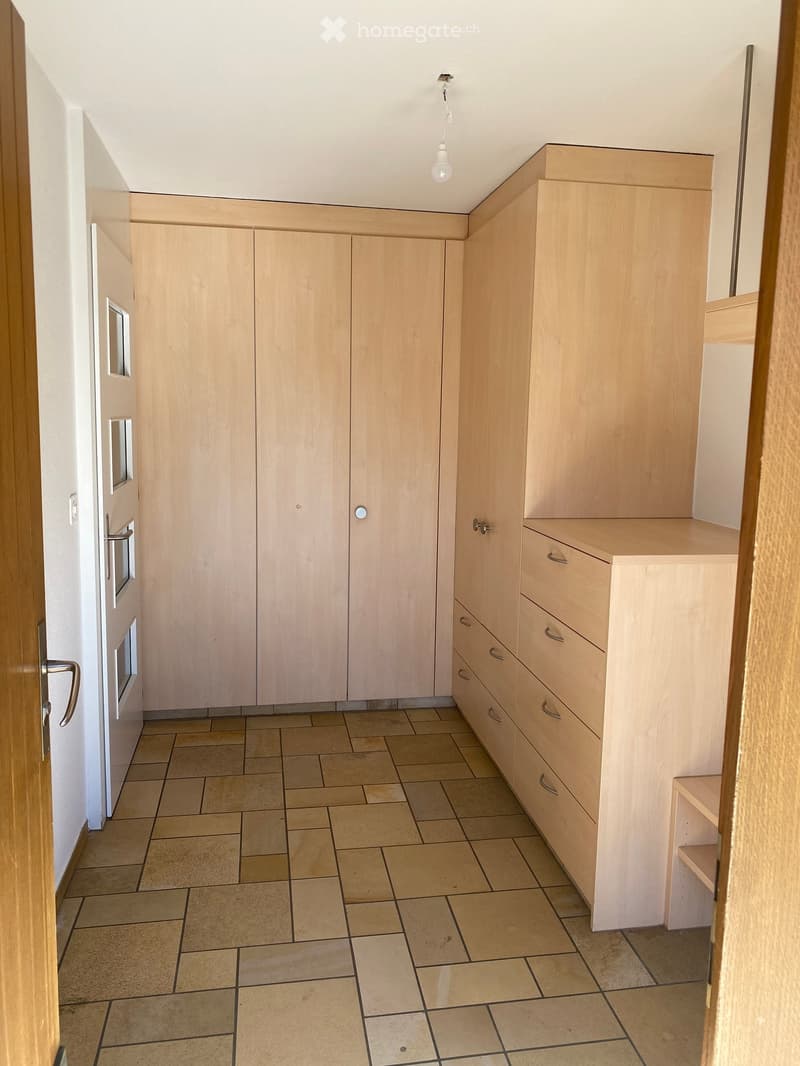 Empty hallway with light wooden built-in wardrobes and tiled floor.