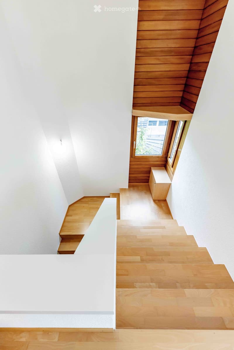 Modern staircase with wooden steps and white walls, featuring a small window at the top landing.