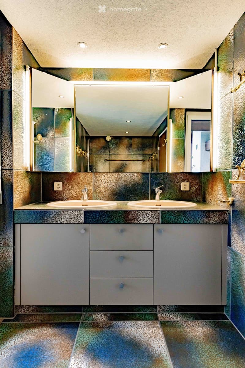 Modern bathroom with two sinks, mirrored cabinet, colorful mosaic tiles, and sleek grey cabinets.