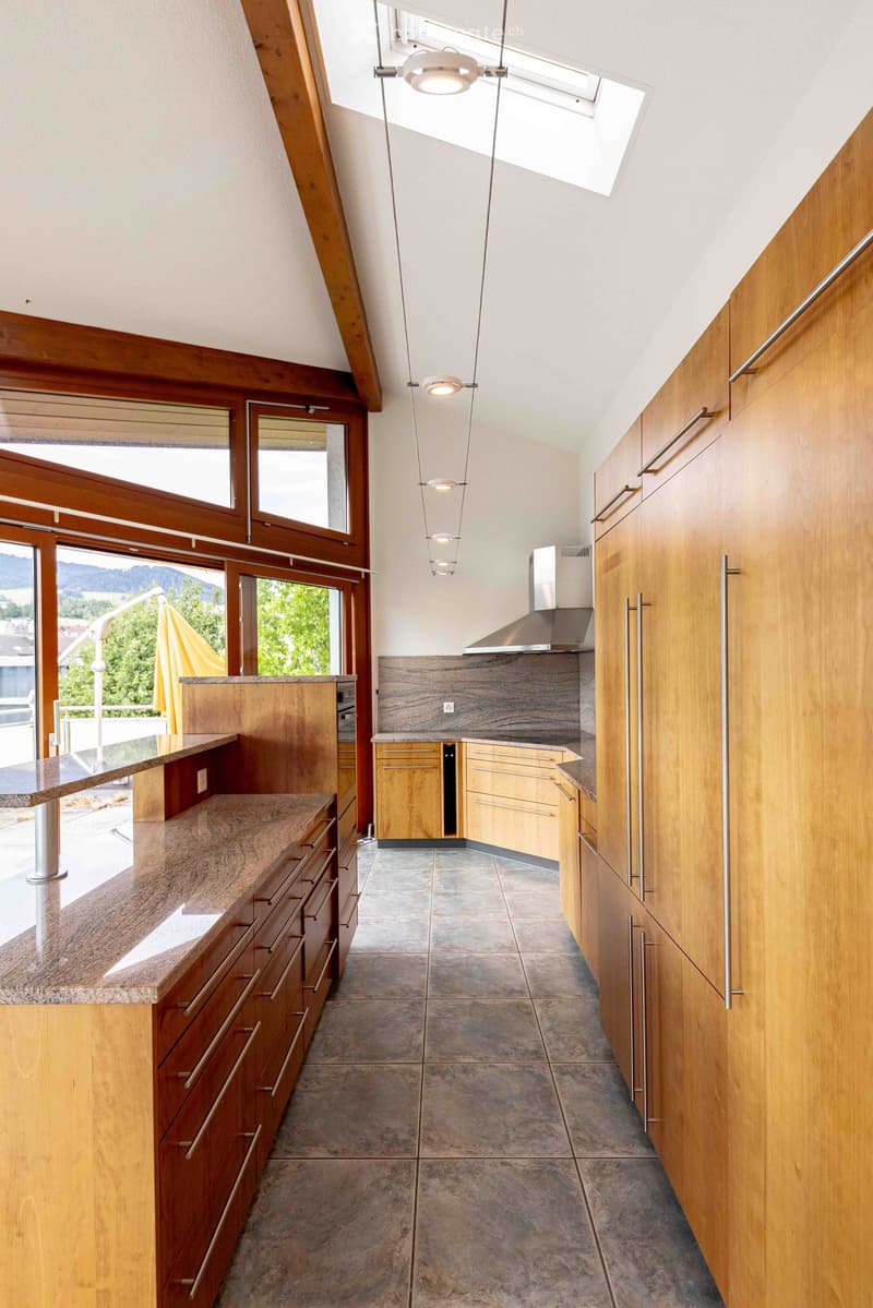 Modern kitchen with wooden cabinets, granite countertop, stainless steel range hood, and pendant lighting.