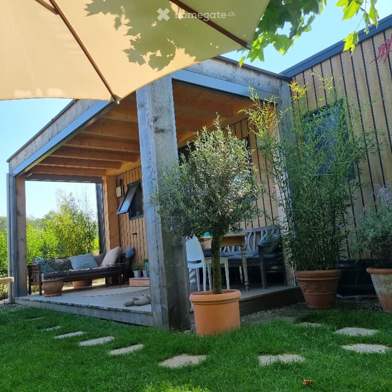 A modern outdoor patio area with wooden decking, a covered seating area, potted plants, and a small bench.