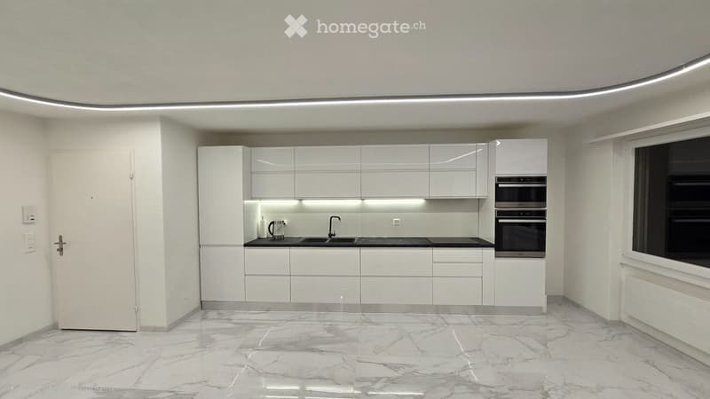 Modern, minimalist kitchen with white cabinets, marble flooring, and built-in appliances including a double oven and a coffee maker on the counter.