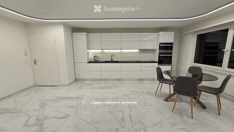Modern kitchen with white cabinets, marble flooring, and a dining area with a glass table and four chairs.