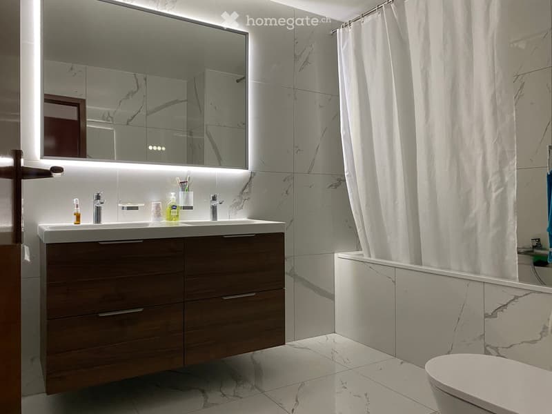 Modern bathroom with marble tiles, double sink vanity, large mirror, bathtub, and shower curtain.