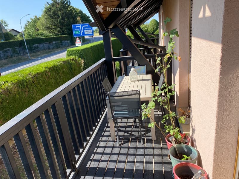 Balcony with wooden decking, metal railing, table, chair, and several potted plants.