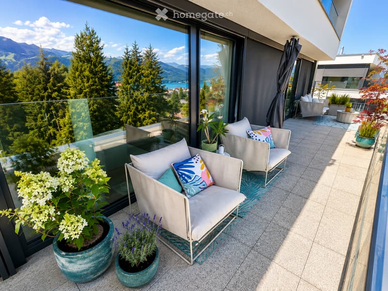 Balcony with a sofa, chairs, a small table, and potted plants, offering a scenic mountain view.