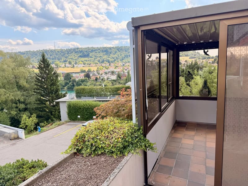 Balcony with tiled floor, large windows, and scenic view of a town and river valley.