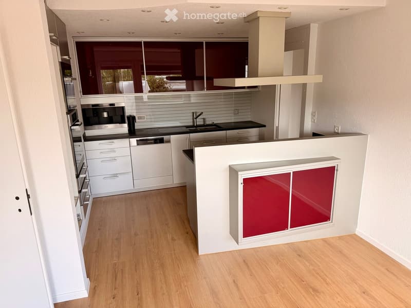 Modern kitchen with white cabinets, stainless steel appliances, and a central island with red accents.