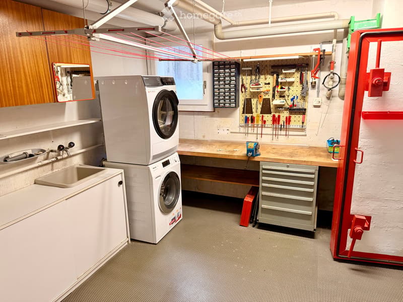 Well-organized utility room with a washing machine, sink, cabinet, tool wall, worktop, toolbox, and mirror.