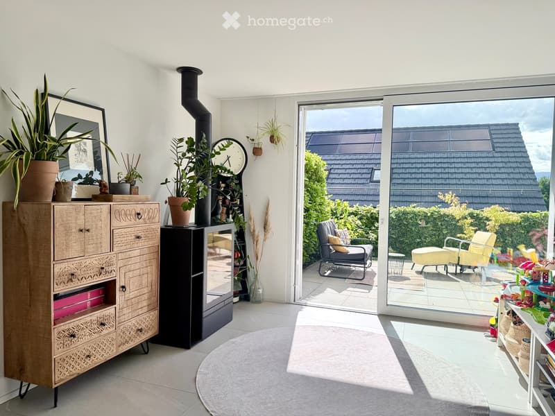 Bright living room with large sliding glass doors leading to a balcony, featuring a wooden cabinet, potted plants, a round rug, and a view of the garden.