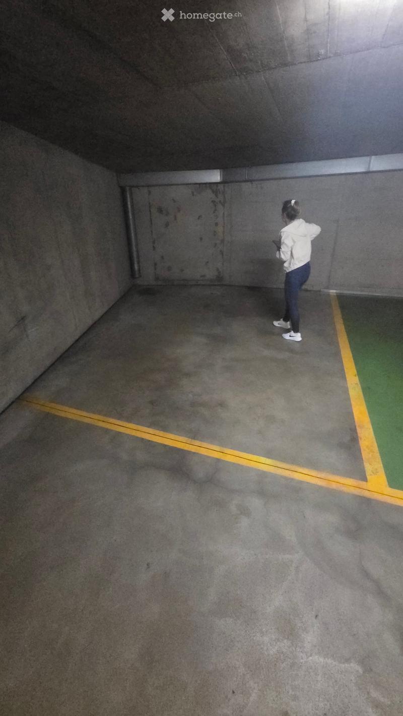 Empty underground parking space with concrete walls and floor, marked parking spaces, and a single person standing near the entrance.