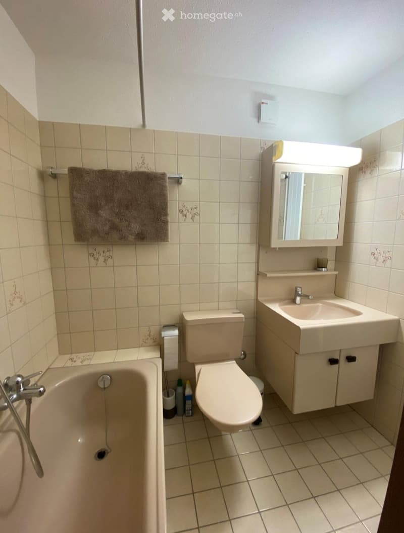 Bathroom with beige tiles, bathtub, toilet, sink with mirror, and a towel hanging on a rack.