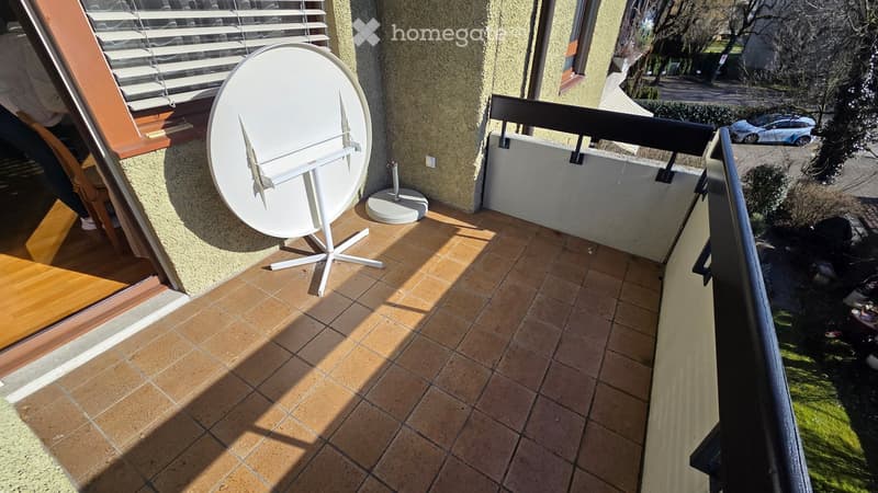 Balcony with tiled floor, satellite dish on stand, metal railing, and view of street and parked cars.