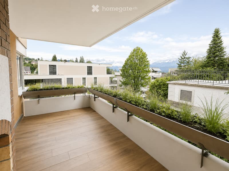 Modern balcony with wooden flooring, integrated planters, and a view of surrounding buildings and greenery.