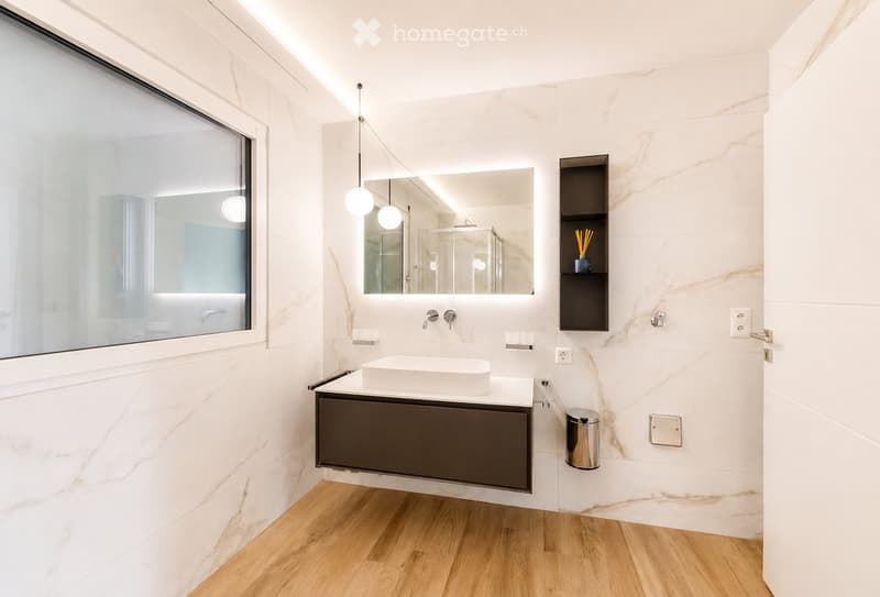 Modern bathroom with white marble walls, wooden floor, floating vanity with dark cabinet, large mirror, and pendant lights.