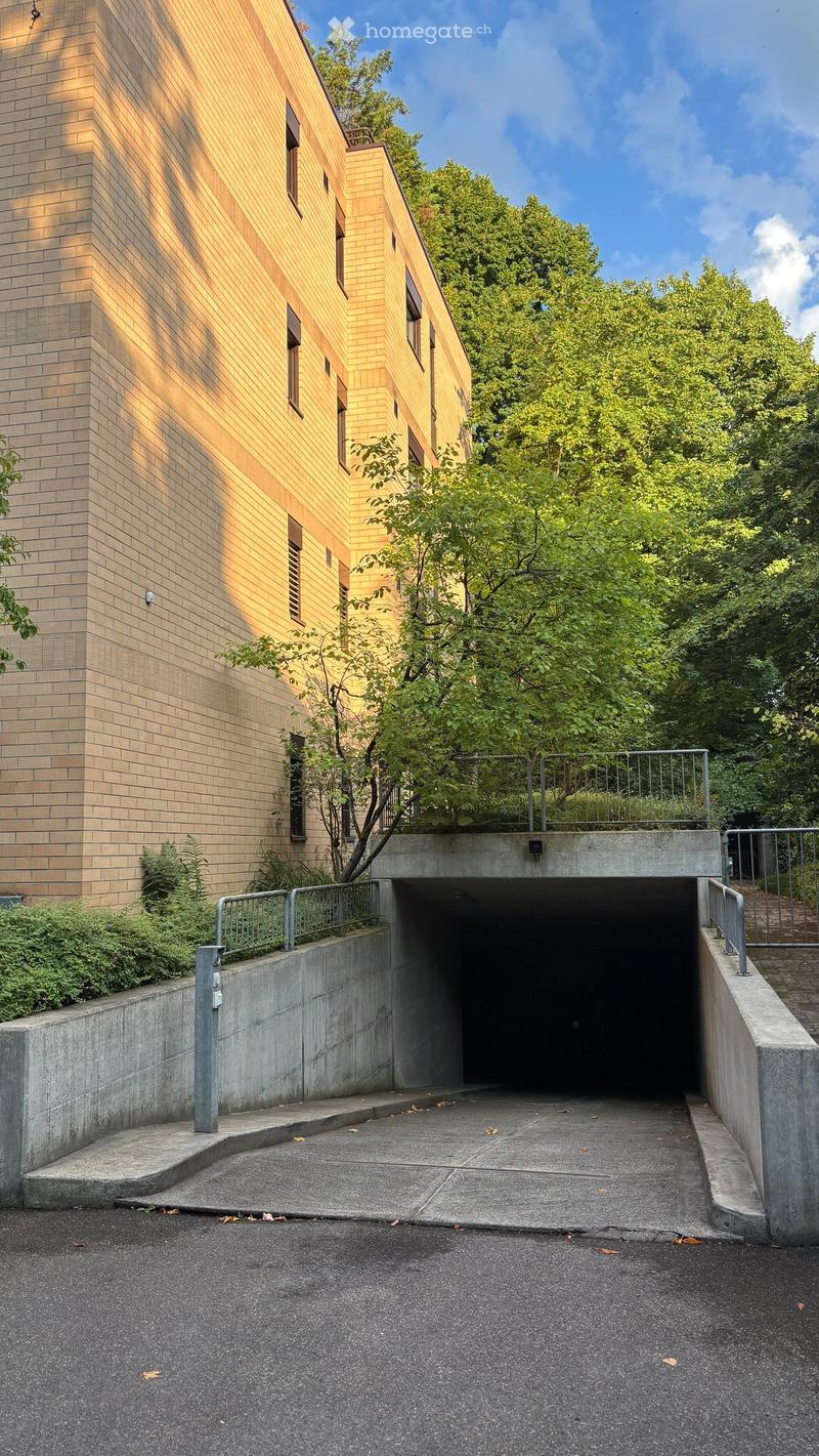 Modern multi-story building with a mix of brick and wood facade, featuring a covered entrance leading to a garage or parking area.