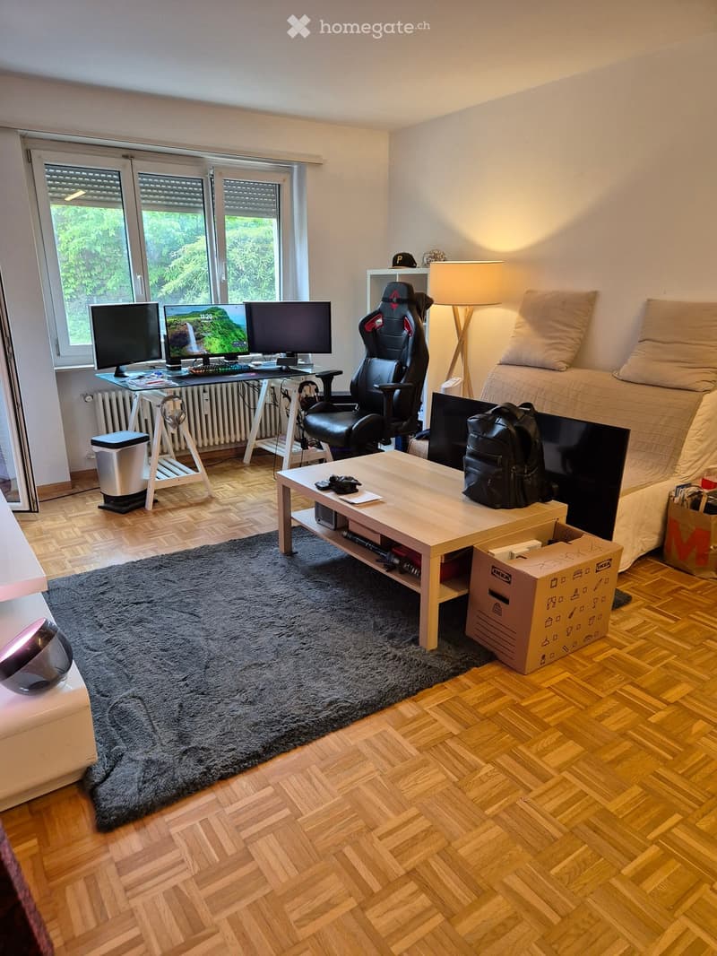 A furnished room with a bed, desk with multiple screens, gaming chair, coffee table, and a large rug on the floor.