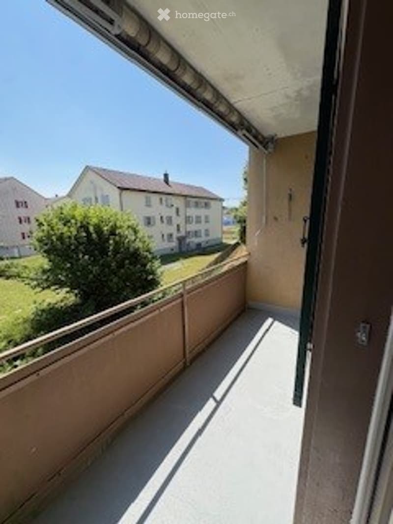 Balcony with metal railing, overlooking a residential area with houses and greenery.