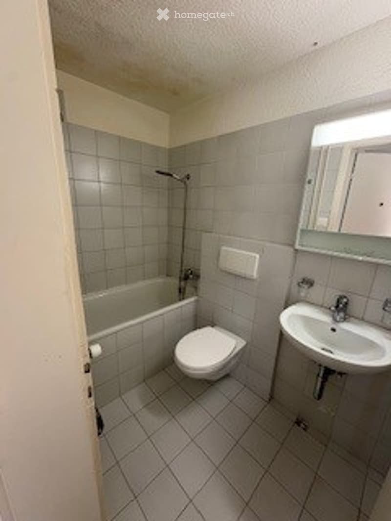 Modern bathroom with tiled walls and floor, featuring a bathtub, toilet, sink, and mirror.
