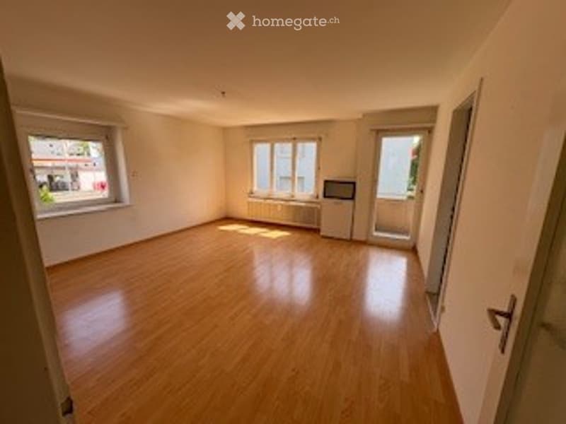 Empty room with wooden flooring, white walls, and large windows. No furniture or equipment present.