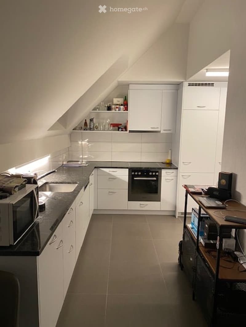 Modern kitchen with white cabinets, black countertop, stainless steel sink, microwave, and oven. Includes a small table with chairs and various kitchen items on shelves.