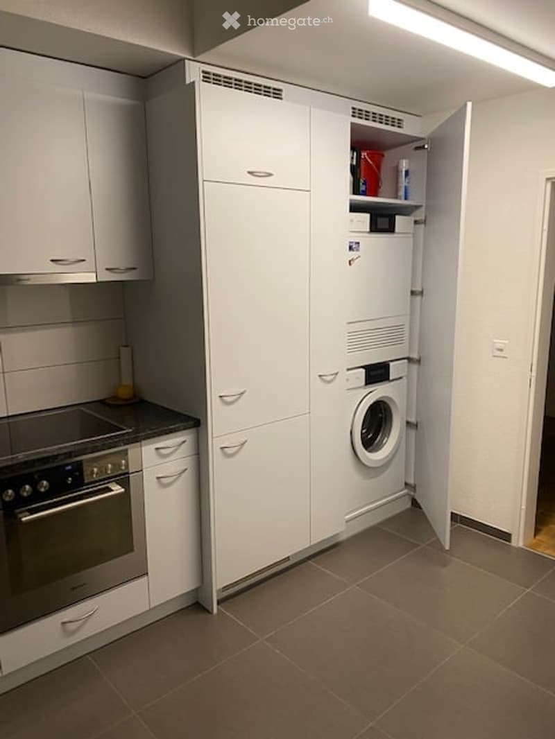 Modern kitchen with white cabinets, a built-in oven, and a compact washing machine in a corner.