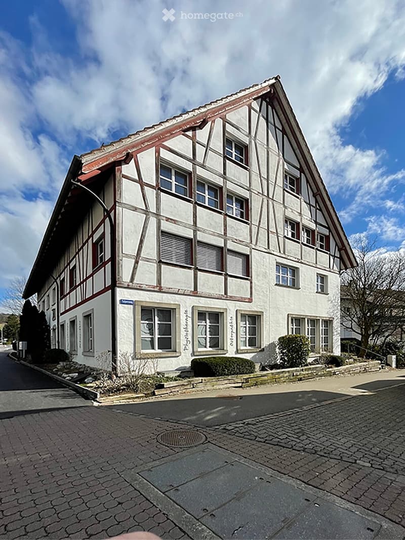 Two-story traditional half-timbered building with white plaster walls and dark wooden beams, multiple windows, and a pitched roof.