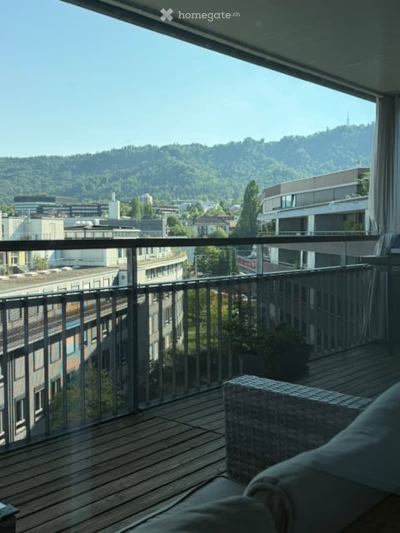 Balcony with wooden decking, metal railing, and a view of the city and surrounding hills.