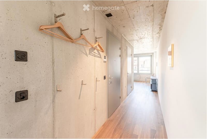 Modern hallway with wooden hangers on the wall, white doors, and a glimpse of an adjacent room with a small table and chair.