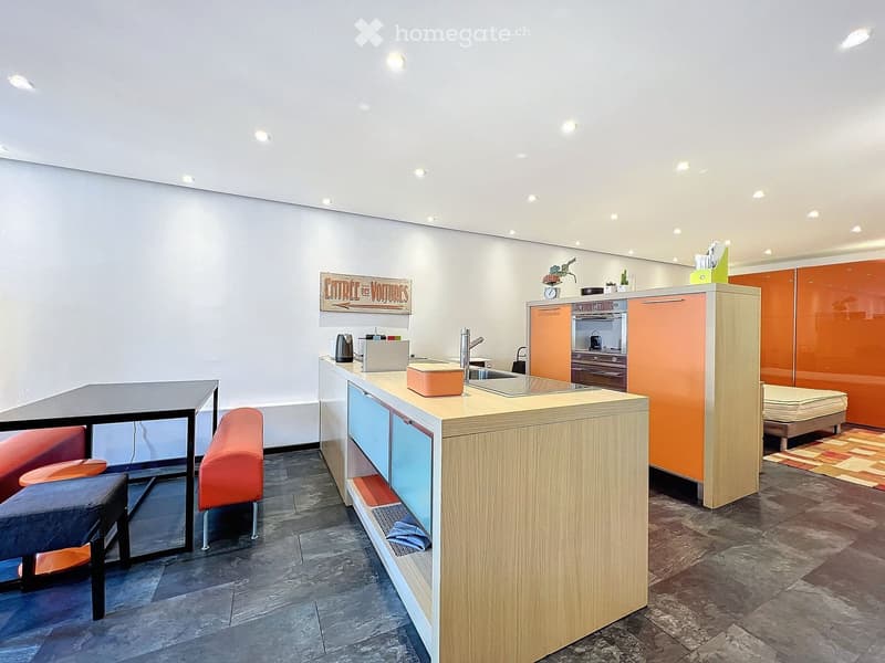Modern kitchen with a central island, sink, and orange cabinets. Includes a small table with chairs, a sign on the wall, and a stool near the island.