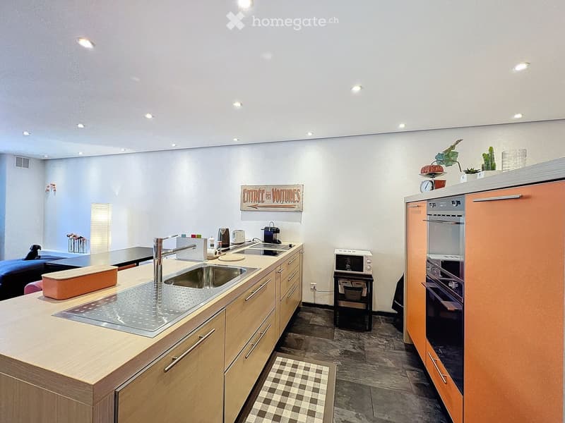 Modern kitchen with wooden cabinets, stainless steel sink, oven, microwave, and coffee maker. Features a small seating area with a table and chairs.