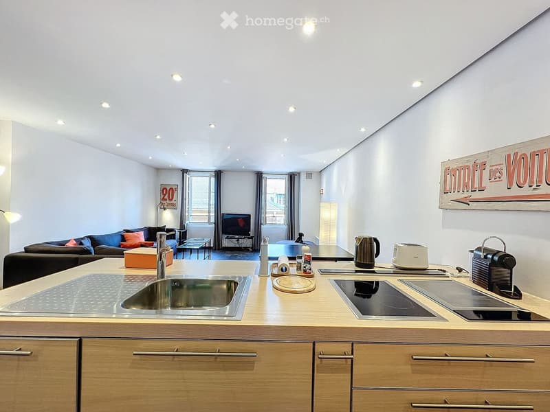 Open-plan living and kitchen area with modern furniture, including a sofa, coffee table, TV, and a kitchen island with appliances.