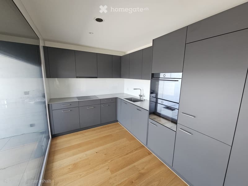 Modern kitchen with grey cabinets, a sink, and an oven, featuring wooden flooring and a large window.