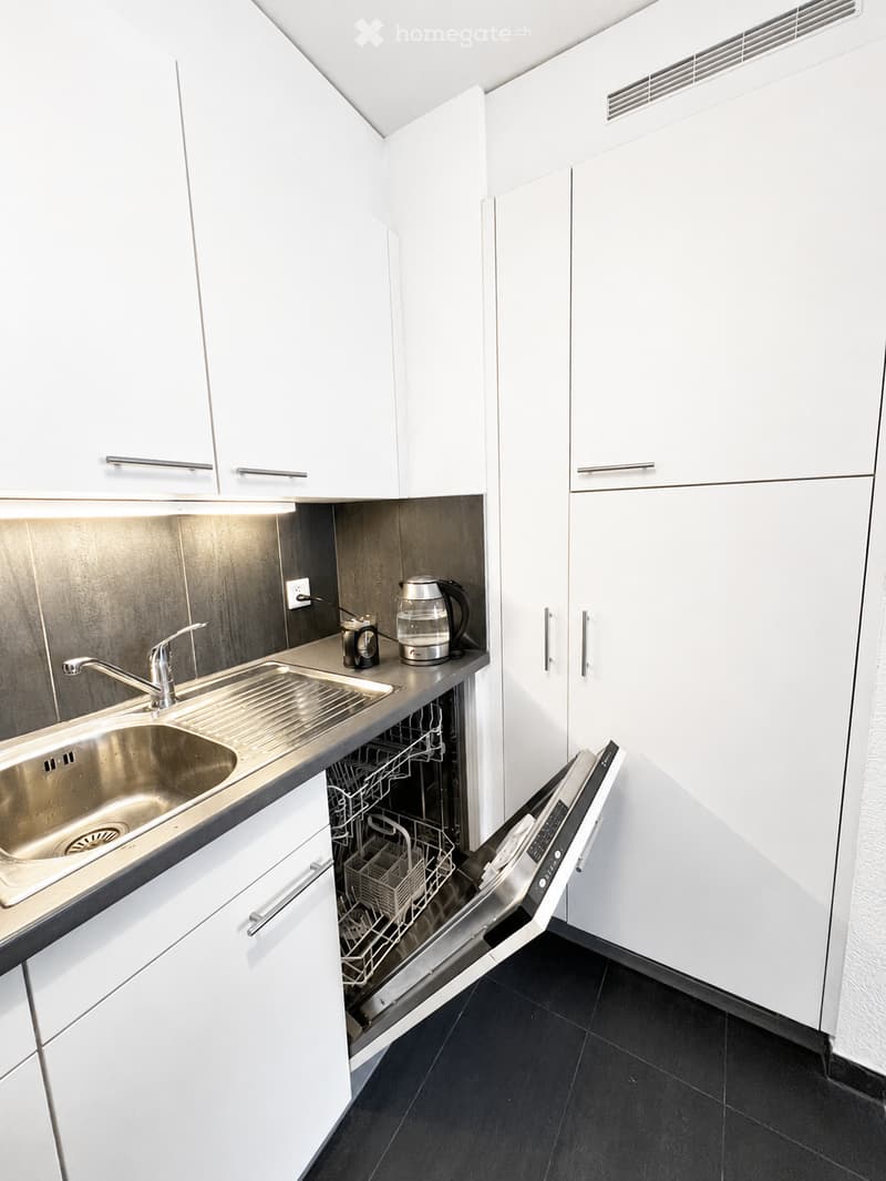 Modern kitchen with white cabinets, stainless steel sink, dishwasher, coffee maker, and electric kettle on the counter.