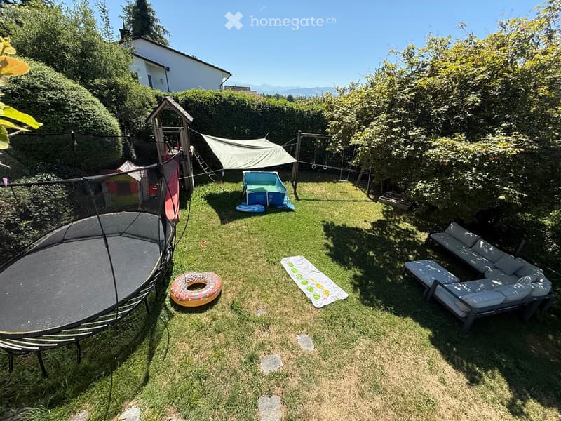 Well-maintained garden with a trampoline, inflatable ring, sun lounger, and outdoor seating area.