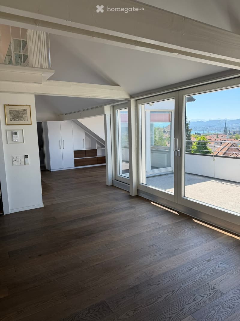 Bright, open room with wooden flooring, large sliding glass doors leading to a balcony, white built-in cabinetry, and a view of the city and mountains.