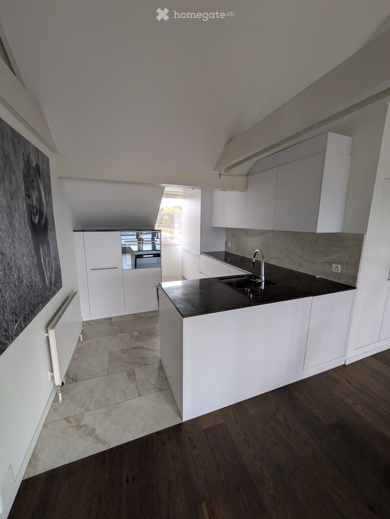 Modern kitchen with white cabinets, black countertop, and stainless steel sink. The space features a mix of tiled and wooden flooring.