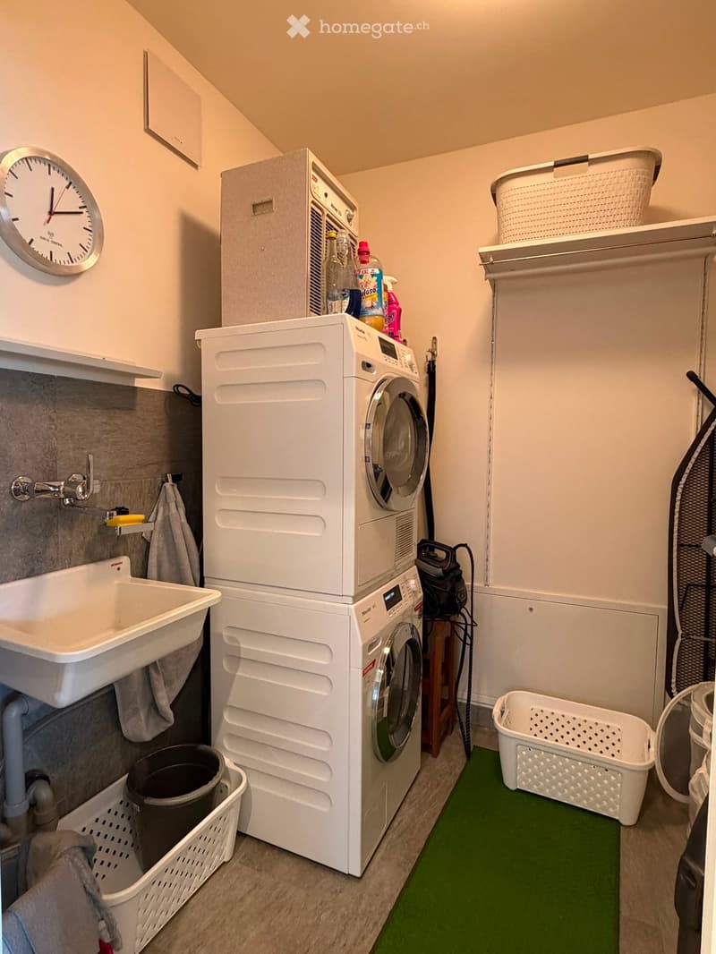 Laundry area with a sink, washing machine, dryer, laundry baskets, and a clock on the wall.