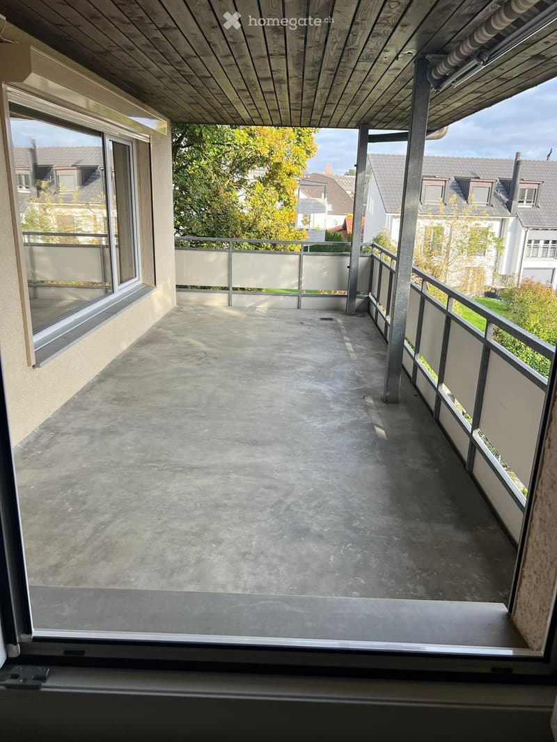 Balcony with metal railings, concrete floor, glass window, view of trees and buildings