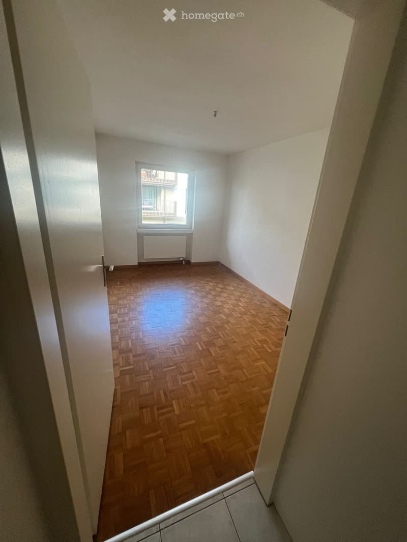 Empty room with wooden floor, white walls, window with balcony, radiator