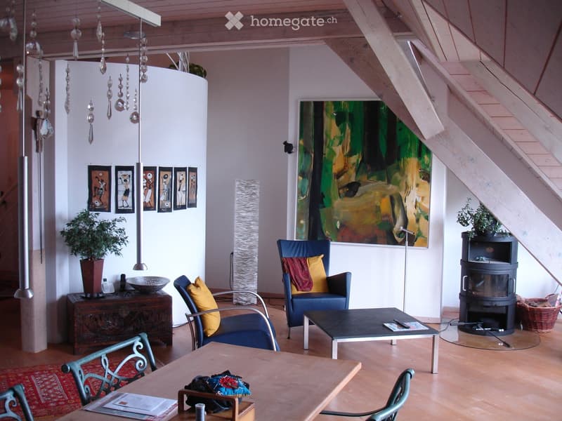Living room with wooden floor, exposed wooden ceiling beams, a fireplace, a sofa, chairs, a coffee table, a dining table, and artwork on the walls.